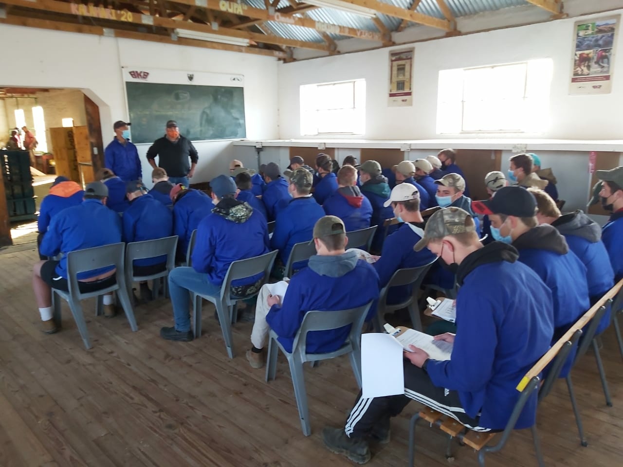 Group of Marlow learners in blue uniforms seated on chairs in a classroom setting, focusing on a presentation by two standing speakers at the front.