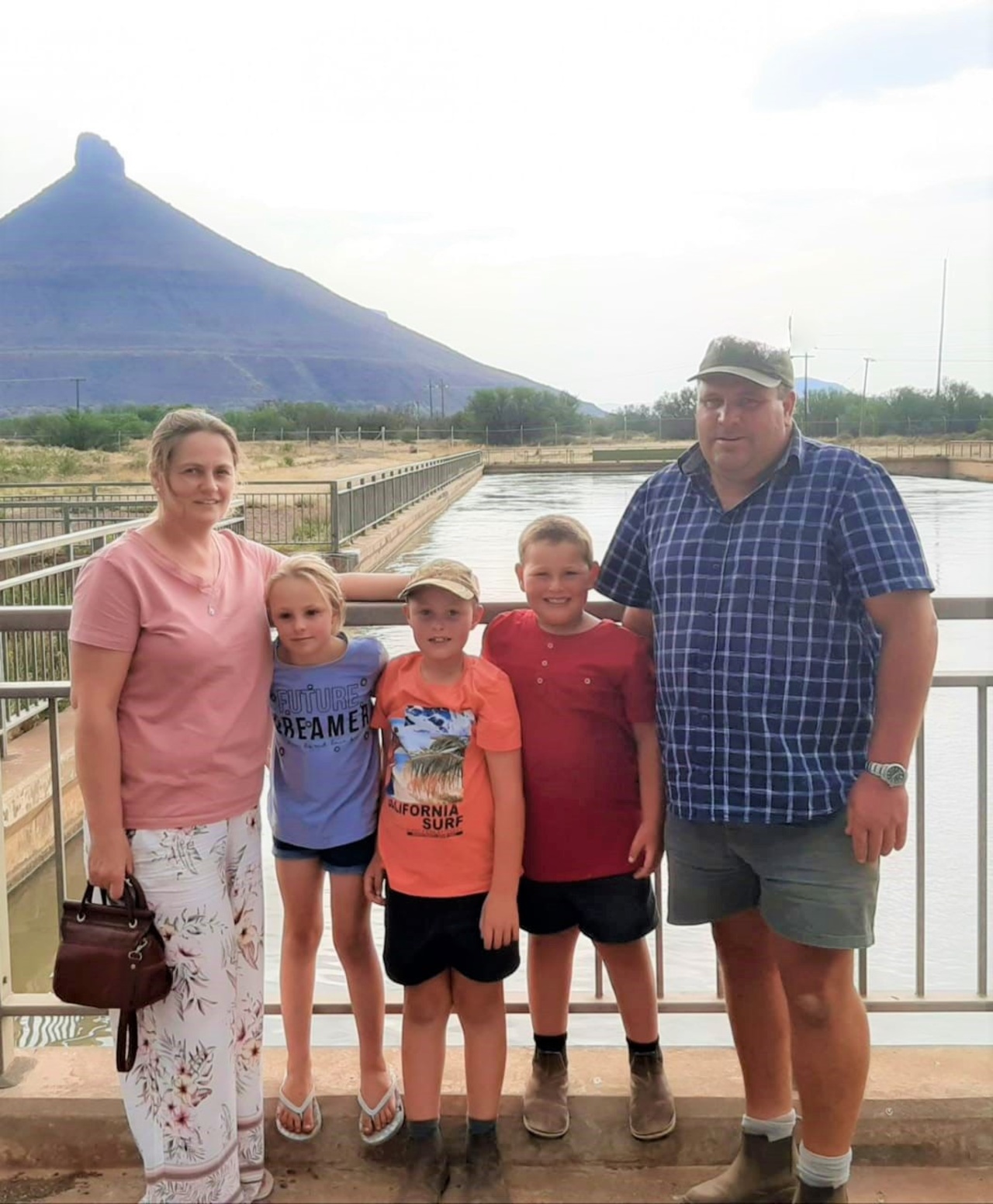 Willem and Soreta Wagener and their three children posing together on a bridge with a mountain in the background.