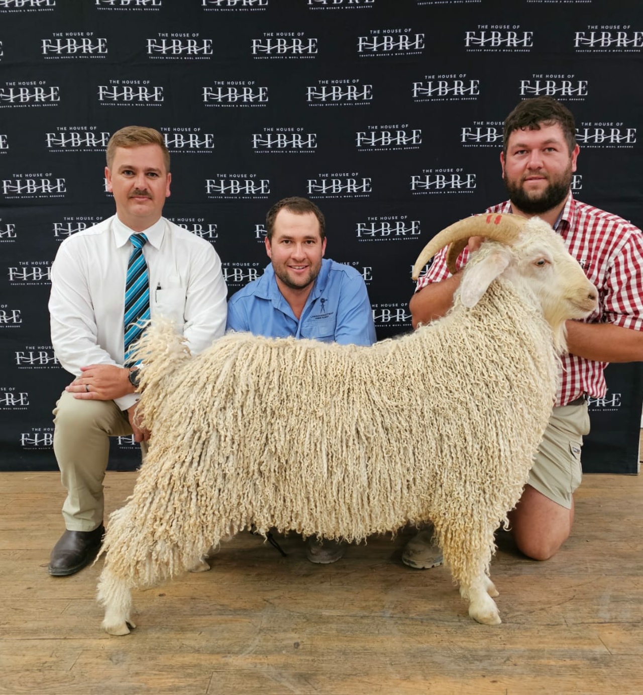 Three individuals posing with a prize-winning Angora goat at an event hosted by House of Fibre.